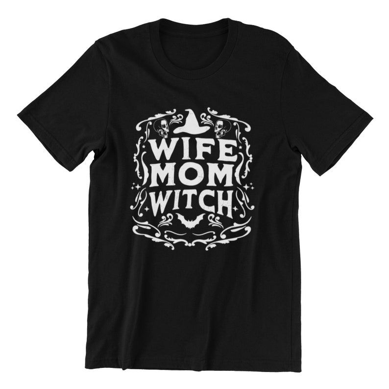 Pu&ograve; includere: Maglietta nera con un design grafico bianco che dice "Wife Mom Witch" con un cappello da strega e teschi.