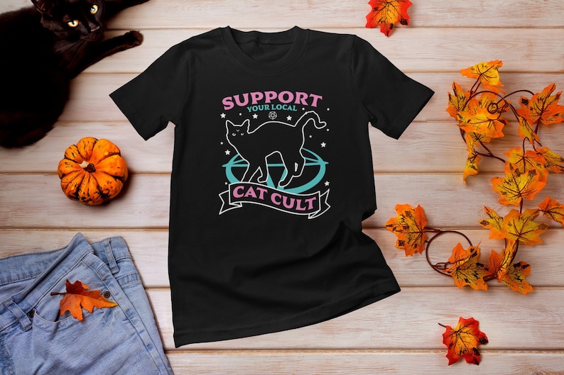 May include: Black t-shirt with a graphic of a black cat standing on a pentagram with stars and the text "Support Your Local Cat Cult".