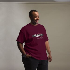 May include: A maroon t-shirt with the text "SELECTIVE" in white and black, with additional text below. The shirt is short-sleeved and appears to be made of a soft material. The overall theme is apparel.