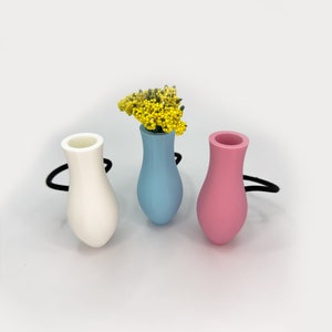 May include: Three small ceramic vases in white, light blue, and pink. The light blue vase has a small bouquet of yellow flowers.