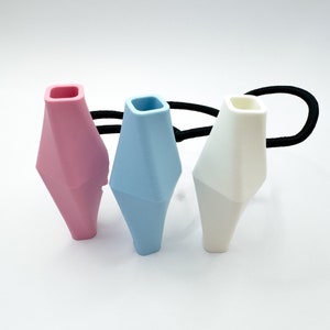 May include: Three hair ties with geometric shaped silicone ends. The hair ties are black and the silicone ends are pink, light blue, and white.
