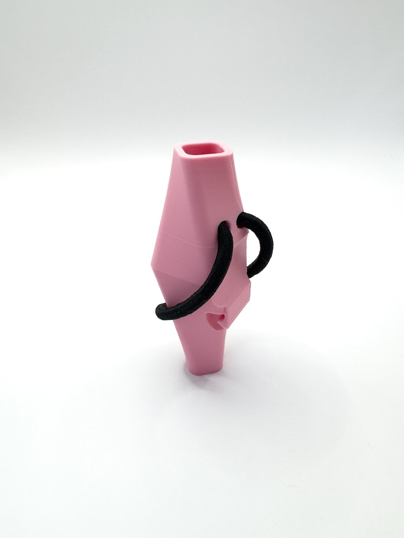 May include: A pink whistle with a black elastic loop attached to the top. The whistle is shaped like a diamond and has a small hole on the side.