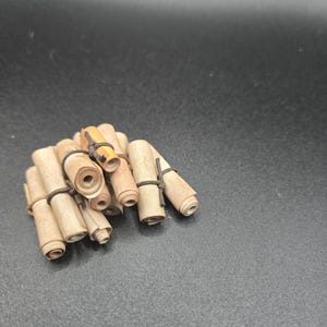 May include: A cluster of small, rolled paper scrolls bound with dark twine. The scrolls are a light tan colour, with some showing a slightly darker, orange hue. The background is a solid, dark grey.
