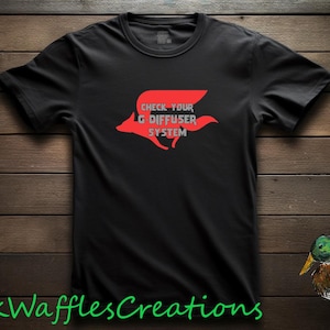 May include: A black short-sleeved t-shirt featuring a red graphic of a stylized animal silhouette with the text "CHECK YOUR G DIFFUSER SYSTEM" printed in gray. The shirt is displayed against a dark wooden background with a mallard duck illustration.
