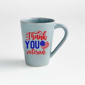 Peut inclure: Une tasse en c&eacute;ramique bleu clair avec une anse incurv&eacute;e. La tasse porte l'inscription "Thank You Veteran" en rouge et bleu, avec un motif de c&oelig;ur drapeau am&eacute;ricain. La tasse est de taille standard.