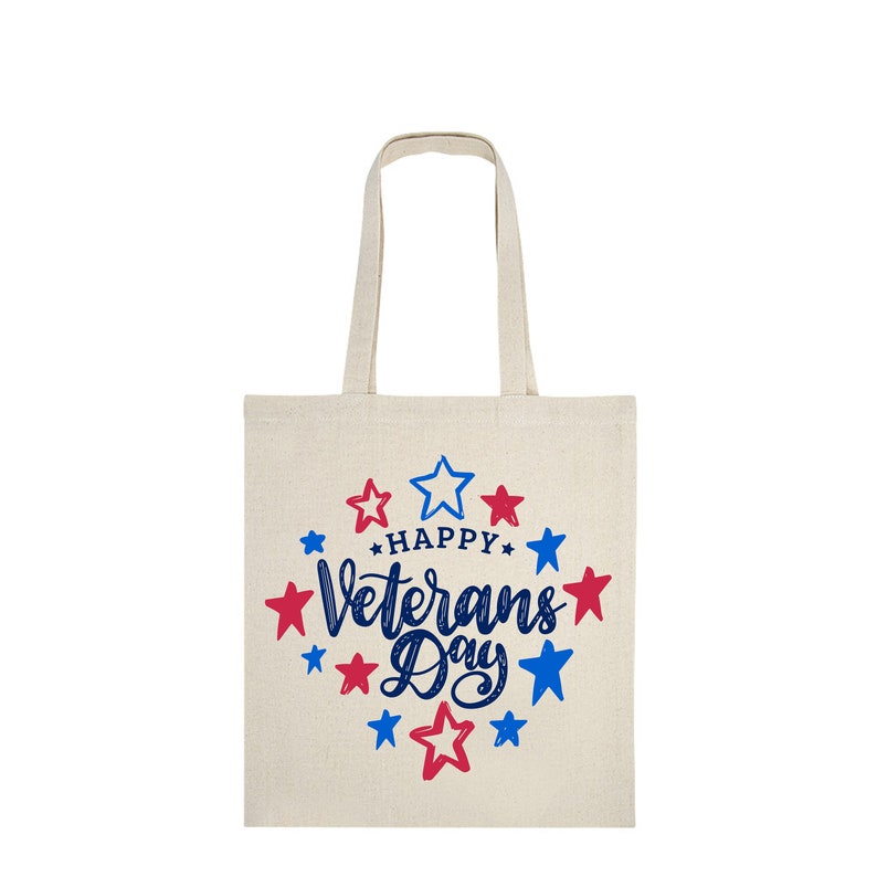 Peut inclure: Un sac fourre-tout en toile beige avec l'inscription "Happy Veterans Day" en bleu, entour&eacute;e d'&eacute;toiles rouges et bleues. Le sac poss&egrave;de deux anses et est con&ccedil;u pour transporter des objets.