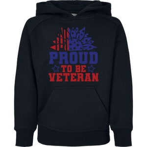 Peut inclure: Un sweat &agrave; capuche bleu marine avec une poche avant. Le motif repr&eacute;sente un tournesol avec des &eacute;l&eacute;ments rouges et bleus, et les mots "PROUD TO BE VETERAN" en rouge et bleu.