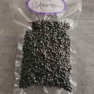 May include: A clear vacuum-sealed plastic bag filled with dark purple freeze-dried elderberries. The oval label at the top reads Rahl Farms, Organically Grown, Freeze-Dried, Elderberries, and Net Weight 2 oz. The berries are small and round.