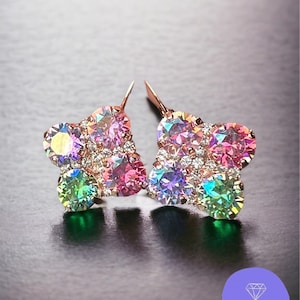 May include: A pair of flower-shaped earrings with iridescent, multi-colored gemstones. The earrings have a rose gold setting and are displayed on a dark surface. The earrings are from Sparkled Rose Jewelry.