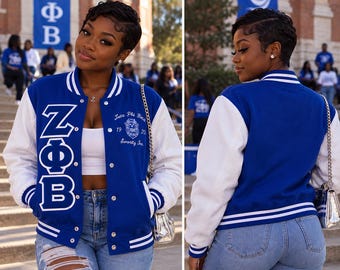May include: A royal blue and white varsity jacket featuring the Greek letters ZΦB embroidered in white on the front left panel. The jacket includes a white embroidered crest with the text Zeta Phi Beta Sorority Inc. 1920 on the front right.