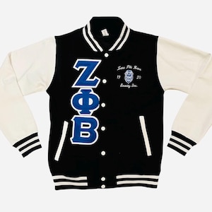 Peut inclure: Veste de style universitaire noire et blanche avec des manches blanches. Elle affiche les lettres grecques ZΦB en bleu, le texte "Zeta Phi Beta" et les années "19" et "20". Les poignets et le col sont rayés de blanc.