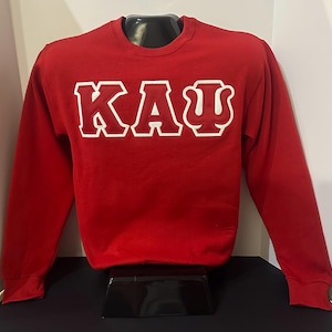 May include: Red sweatshirt with white lettering that reads "KAU" in a collegiate style font.
