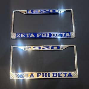 May include: Two silver license plate frames with blue enamel. The top frame says "1920" and "Zeta Phi Beta". The bottom frame says "1920" and "Zeta Phi Beta".