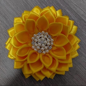 以下が含まれることがあります： パールとラインストーンのセンターが付いた黄色のサテンの花。花は約7.5cmの直径です。