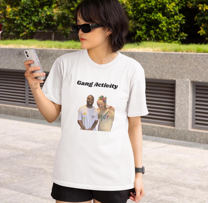 K&ouml;nnte beinhalten: Wei&szlig;es T-Shirt mit einem schwarzen grafischen Aufdruck von zwei Personen. Der Text "Gang Activity" ist &uuml;ber dem Aufdruck gedruckt.