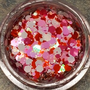 May include: A small container filled with red, pink, and white glitter. The glitter is in various shapes and sizes.