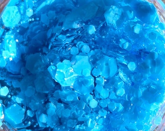 May include: A close-up of a jar filled with bright blue glitter. The glitter is made up of small, irregular shapes.