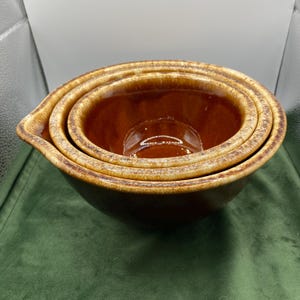 May include: Set of four brown and beige ceramic mixing bowls. The bowls are nested inside each other, with the largest bowl at the bottom and the smallest bowl at the top.