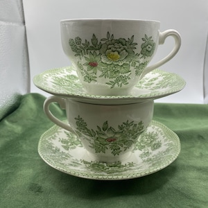 May include: Two white teacups and saucers with a green floral pattern. The cups and saucers are stacked on top of each other.