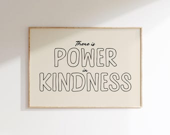 May include: A framed print with the words "There is POWER in KINDNESS" in black, outlined letters. The background is a light beige color, and the frame is a light wood color. The print is hanging on a white wall.