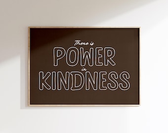 May include: A framed print with the words "There is POWER in KINDNESS" in white, outlined letters on a dark brown background. The frame is a light brown color, and the print is hanging on a white wall.
