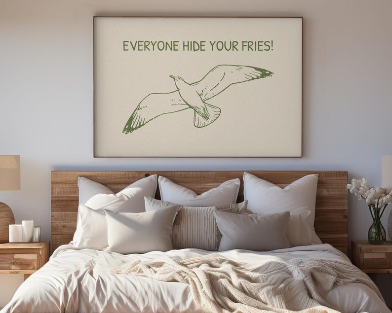 Pode incluir: Uma impress&atilde;o emoldurada com uma ilustra&ccedil;&atilde;o verde de uma gaivota em voo e o texto "EVERYONE HIDE YOUR FRIES!". A obra de arte est&aacute; acima de uma cama com roupa de cama em tons neutros.