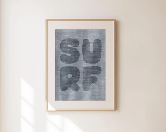 May include: Framed wall art with the word "SURF" in large, rounded, dark gray letters. The letters have a textured appearance, set against a light gray background. The artwork is in a light wood frame, hanging on a cream-colored wall.