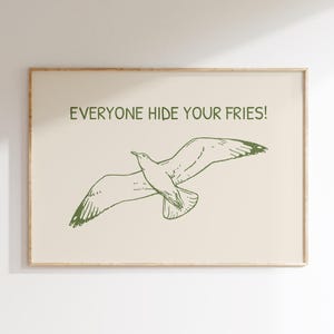 Pode incluir: Uma impress&atilde;o art&iacute;stica emoldurada com uma ilustra&ccedil;&atilde;o de gaivota verde sobre um fundo creme. O texto "EVERYONE HIDE YOUR FRIES!" est&aacute; impresso acima. A obra de arte tem um estilo simples e minimalista.