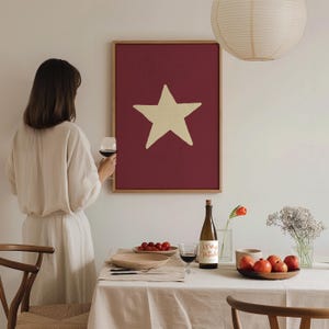 Pu&ograve; includere: Un dipinto incorniciato con una grande stella gialla su uno sfondo bordeaux. Una bottiglia di vino con un'etichetta che recita "Anna Paula" &egrave; su un tavolo con una tovaglia bianca. Ci sono uva rossa, un bicchiere di vino rosso e una ciotola di mele rosse sul tavolo.