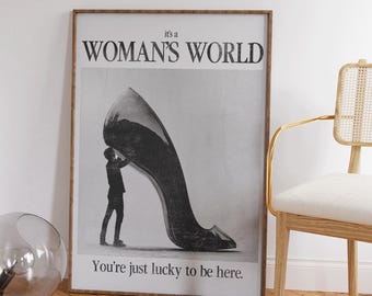 May include: A black and white poster featuring a man holding up a giant high-heeled shoe. The poster reads "It's a Woman's World" and "You're just lucky to be here."