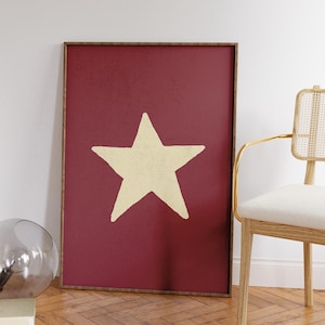 Pu&ograve; includere: Una stampa incorniciata con una grande stella color crema su uno sfondo rosso scuro.