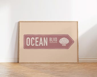 May include: A pink and white sign with the text "Ocean Blvd" and a seashell graphic. The sign is framed in a light wood frame.