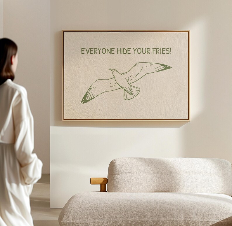 Pode incluir: Impress&atilde;o em tela emoldurada com uma ilustra&ccedil;&atilde;o de gaivota verde e o texto &laquo;EVERYONE HIDE YOUR FRIES!&raquo;. A obra de arte &eacute; emoldurada em uma moldura de madeira e pendurada em uma parede de cor neutra.