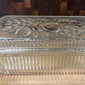 May include: Clear glass rectangular baking dish with a lid. The lid features a raised fruit design. The dish has vertical ribbed sides and is suitable for baking and serving.