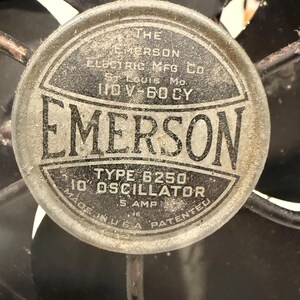 Puede incluir: Primer plano de un ventilador el&eacute;ctrico Emerson antiguo. El emblema central es circular con el nombre "EMERSON" en un lugar destacado. El texto incluye "TYPE 6250 10" OSCILLATOR" y "MADE IN U.S.A."