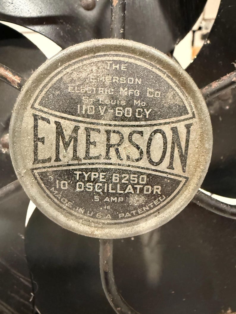 Puede incluir: Primer plano de un ventilador el&eacute;ctrico Emerson antiguo. El emblema central es circular con el nombre "EMERSON" en un lugar destacado. El texto incluye "TYPE 6250 10" OSCILLATOR" y "MADE IN U.S.A."