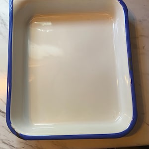 May include: A white enamel baking dish with a blue rim. The dish is rectangular and has a slightly rounded edge.