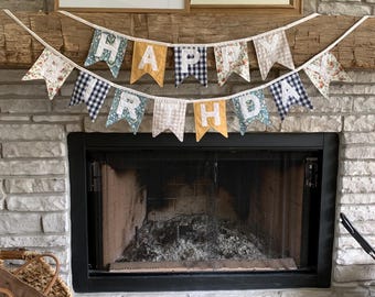 May include: A fabric banner featuring two rows of pennants spelling out HAPPY BIRTHDAY. The pennants are made from various patterned fabrics including blue and white gingham, floral prints, and solid mustard yellow, with white letters stitched on.