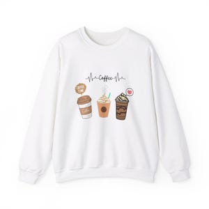 Puede incluir: Sudadera blanca con un gráfico de temática de café. El gráfico presenta tres bebidas de café con el texto "Coffee Time" y "Coffee" con un corazón.