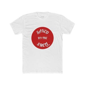 May include: White t-shirt with a red circle graphic. The graphic features the words "SAVED BY THE SMELL" in white, stylized font. The shirt is made of a soft, comfortable material.