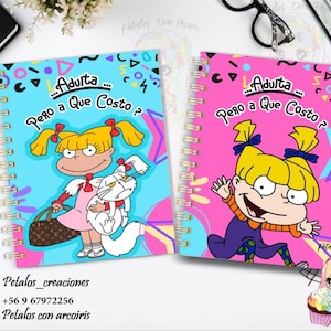 May include: Two pink and blue spiral bound notebooks with a cartoon image of a girl with blonde hair and a white cat. The text on the notebooks reads "...Adulta... Pero a Que Costo?"
