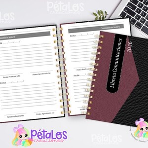 Puede incluir: Una agenda de espiral con una cubierta burdeos y negra, etiquetada como "Libreta Comunicaciones 2026". Las páginas abiertas muestran secciones rayadas para notas y fechas. Un portátil y una taza de café están en el fondo.