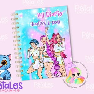 Peut inclure: Cahier à spirales avec une couverture colorée représentant trois personnages de dessins animés tenant des microphones. La couverture indique "Mi Diario Huntrix k-pop" en rose et bleu. Un chat bleu est à gauche.