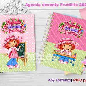 Puede incluir: Dos agendas docentes A5 con encuadernación en espiral tituladas Agenda Docente Frutillita 2027. Las portadas muestran a una niña de dibujos animados con pelo rojo y sombrero de fresa, de pie junto a una pizarra o sentada en un escritorio.