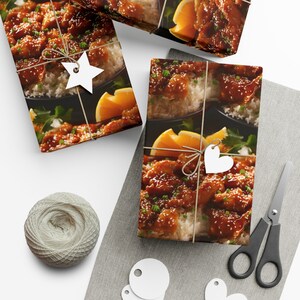 Può includere: Carta da regalo con un primo piano di pollo all'arancia con semi di sesamo e riso bianco. La carta da regalo è legata con uno spago e decorata con etichette bianche a forma di stella e cuore.