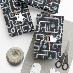 May include: Three gift boxes wrapped in black and silver patterned wrapping paper with a repeating design of pipes. The boxes are tied with twine and decorated with white paper stars and hearts.
