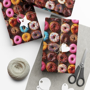 Puede incluir: Papel de regalo con un patrón colorido de donas con varios ingredientes. Los regalos envueltos están atados con hilo y adornados con etiquetas en forma de estrella y corazón. También hay un ovillo de hilo, tijeras y etiquetas en blanco.