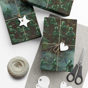 May include: Three wrapped gifts with green toy soldier-themed wrapping paper. Each package is tied with twine and adorned with a white star or heart-shaped tag. A ball of twine, scissors, and gift tags are also present.