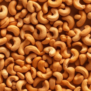 Puede incluir: Una imagen de primer plano de un montón de anacardos. Las nueces son de color marrón claro y tienen una forma ligeramente irregular.