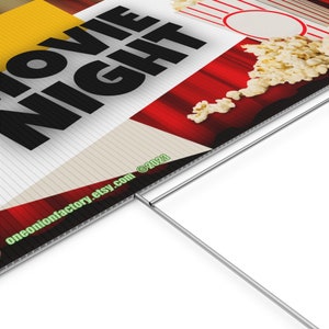 May include: A red and white striped sign with the text "Movie Night" in black letters. The sign has a red curtain background with popcorn spilling out. The sign is made of corrugated plastic and has a metal stake for displaying.